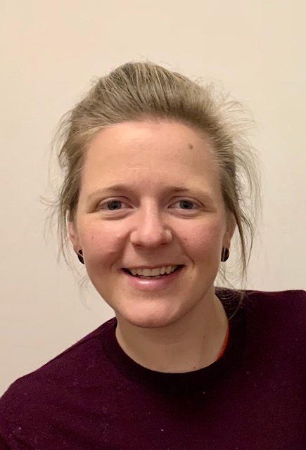 Portrait of young woman with blond hair and wearing maroon shirt and black earrings