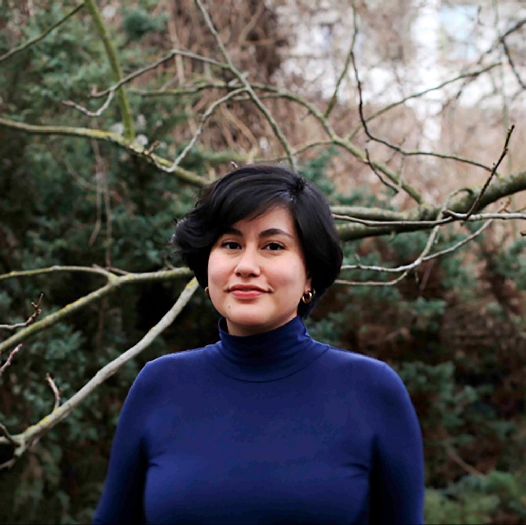 picture of young female with short black hair, gold hoop earrings and blue turtleneck sweater