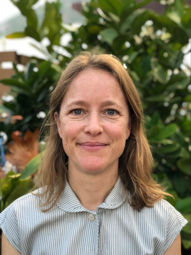 picture of female with short blond hair and blue eyes, wearing a striped white and grey shirt