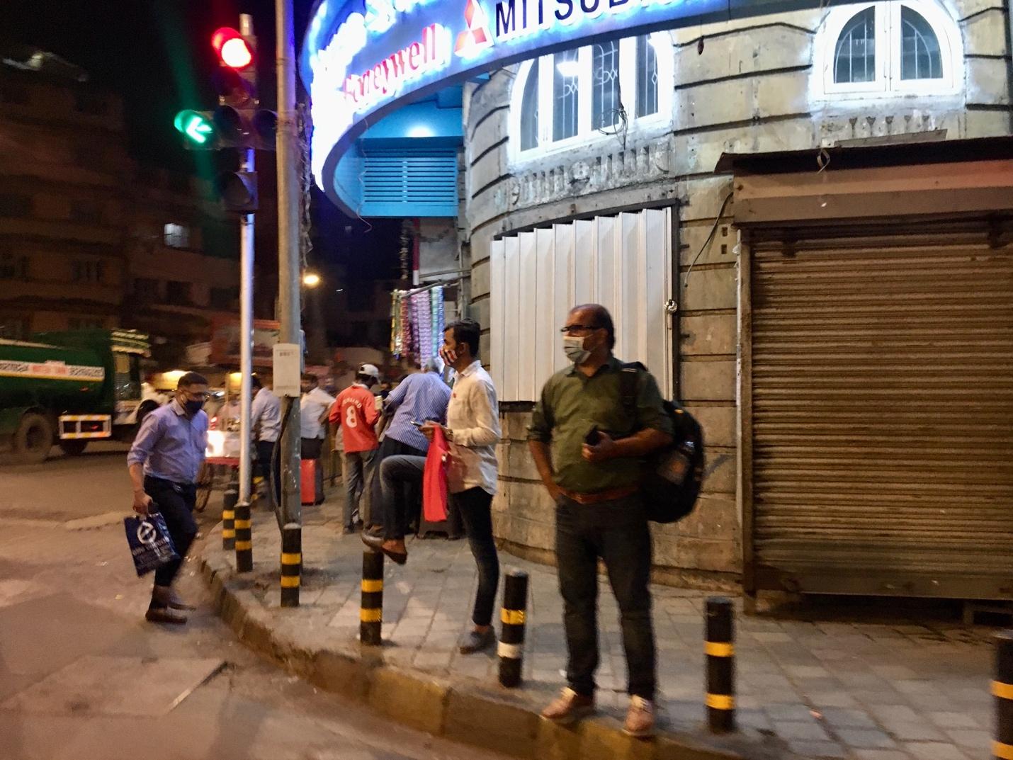 Image of people standing on the pavement by a traffic light, wearing facemasks