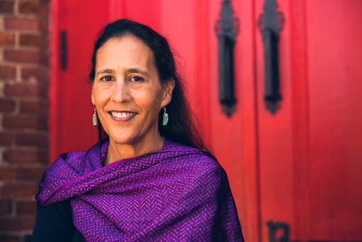 photograph of a woman of colour, Julie Quiroz, wearing a purple shawl against a red background