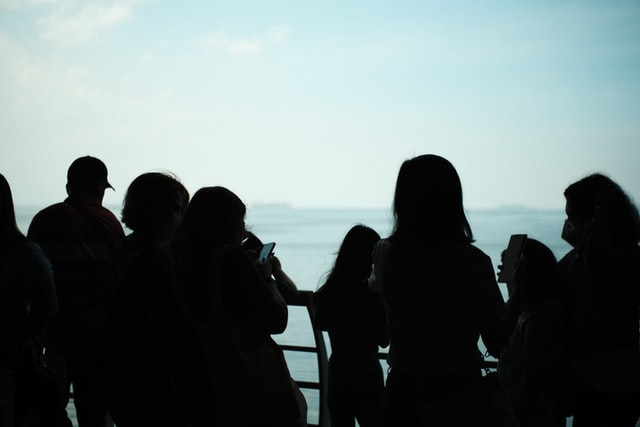 photo of blurry human figures tanding on a platform, the sea is in the background